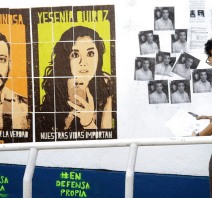 Una imagen de un activista colgando folletos en blanco y negro con retratos impresos en la pared y los grandes retratos de Yesenia y Rubén colgados a su izquierda en la pared.