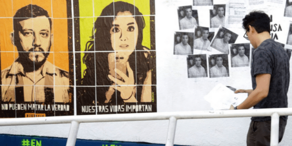 Una imagen de un activista colgando folletos en blanco y negro con retratos impresos en la pared y los grandes retratos de Yesenia y Rubén colgados a su izquierda en la pared.