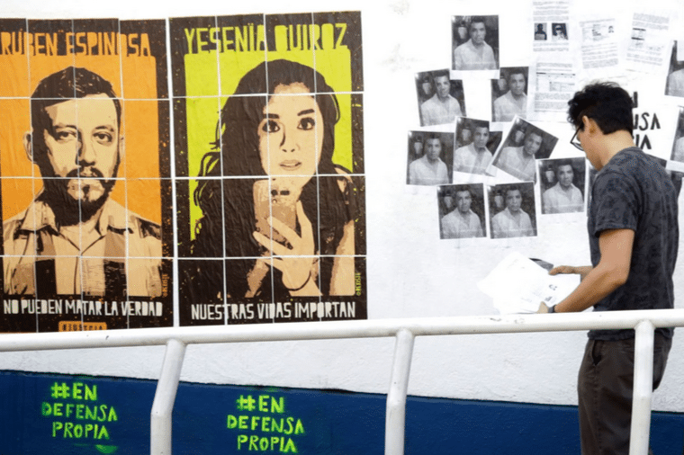 Una imagen de un activista colgando folletos en blanco y negro con retratos impresos en la pared y los grandes retratos de Yesenia y Rubén colgados a su izquierda en la pared.